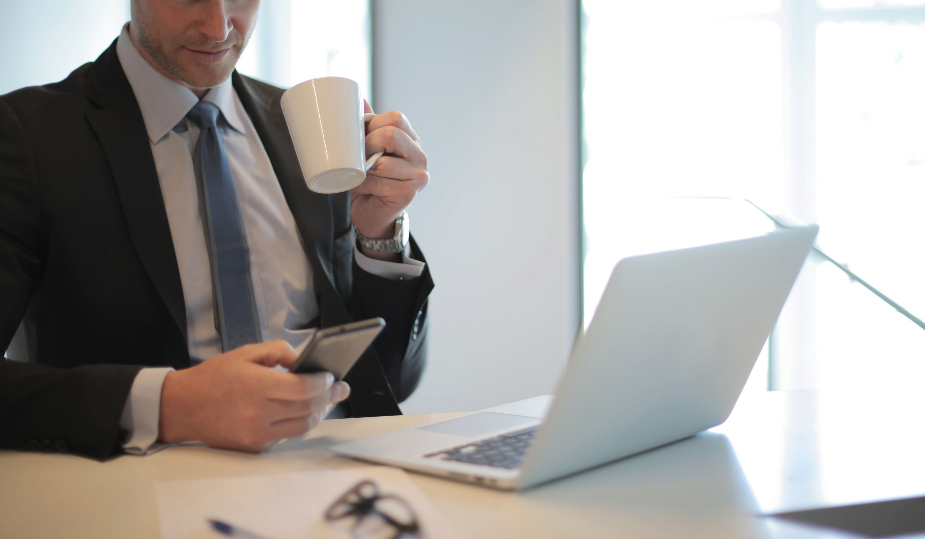 Man drinking coffee and working on phone and laptop