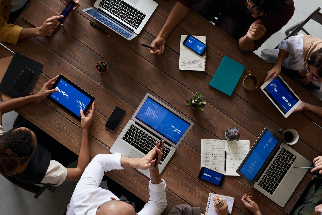 Overhead image of multiple people working on laptops, phones, and tablets together at a table