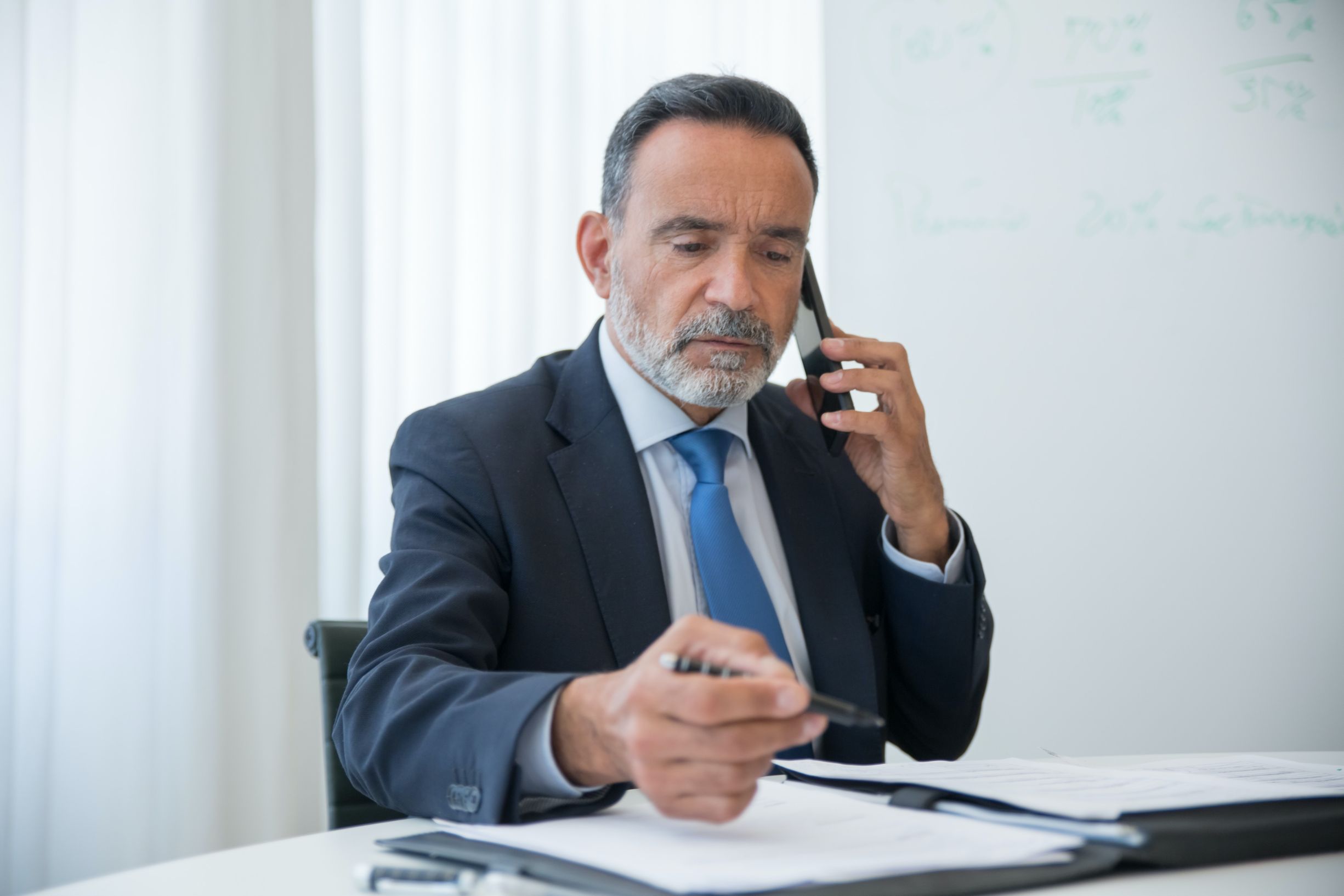 Man talking on phone while on writing a notebook 