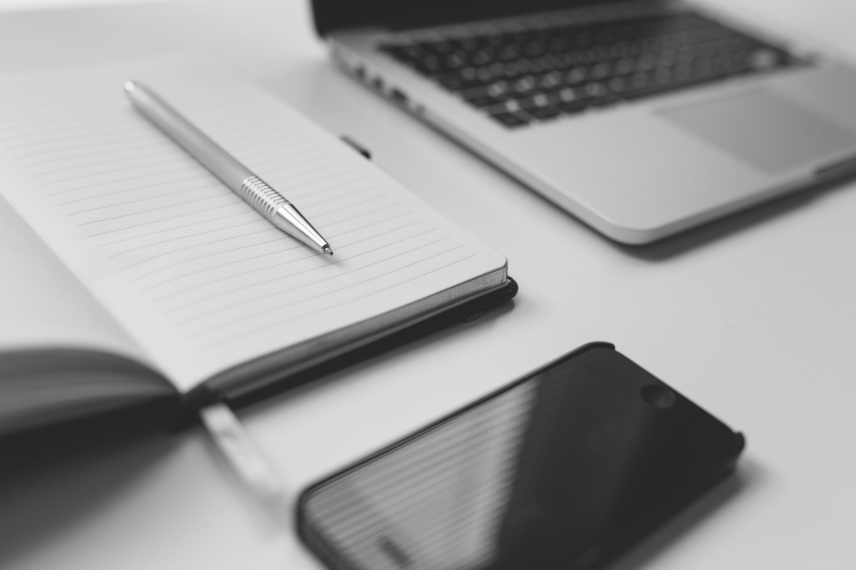 Black IPhone next to laptop and notepad