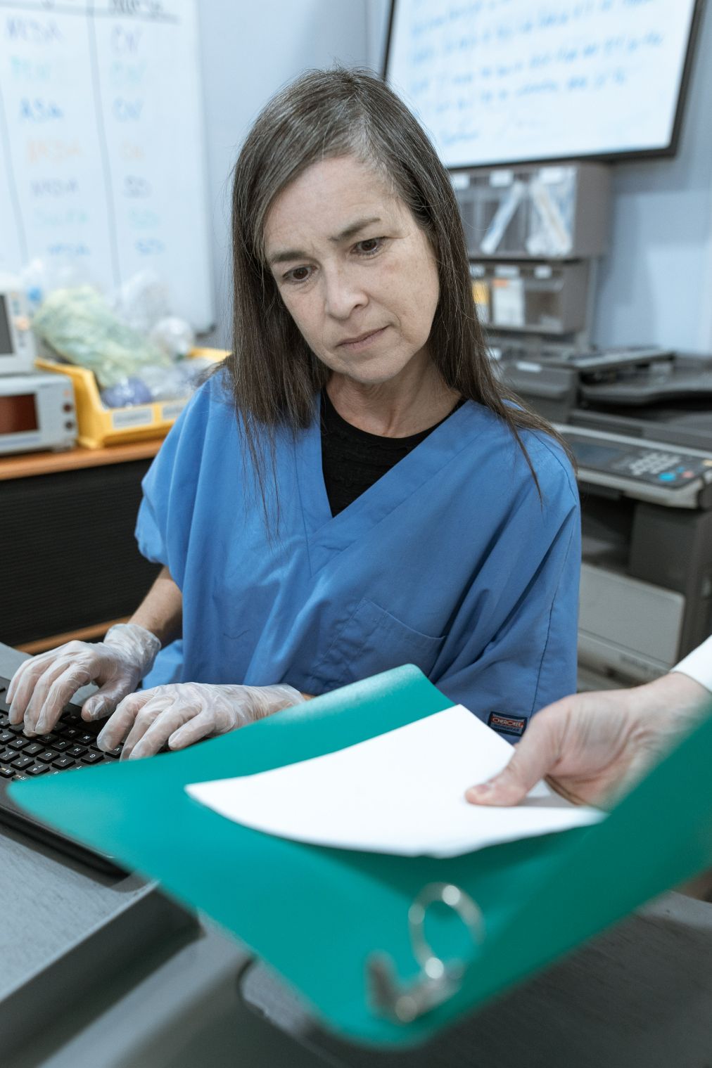 Nurse looking at document and typing on computer