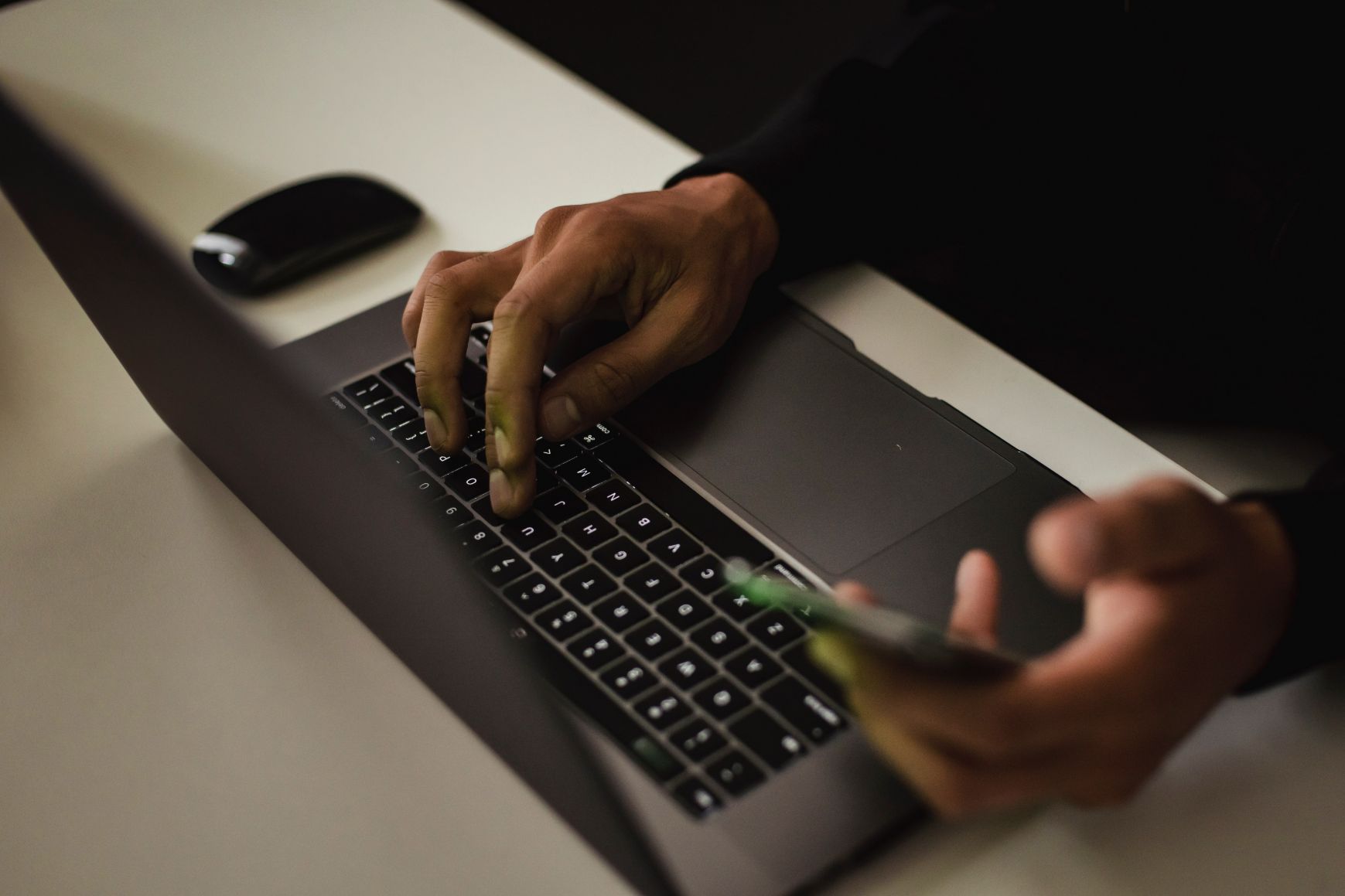 Hands typing on computer and holding a phone