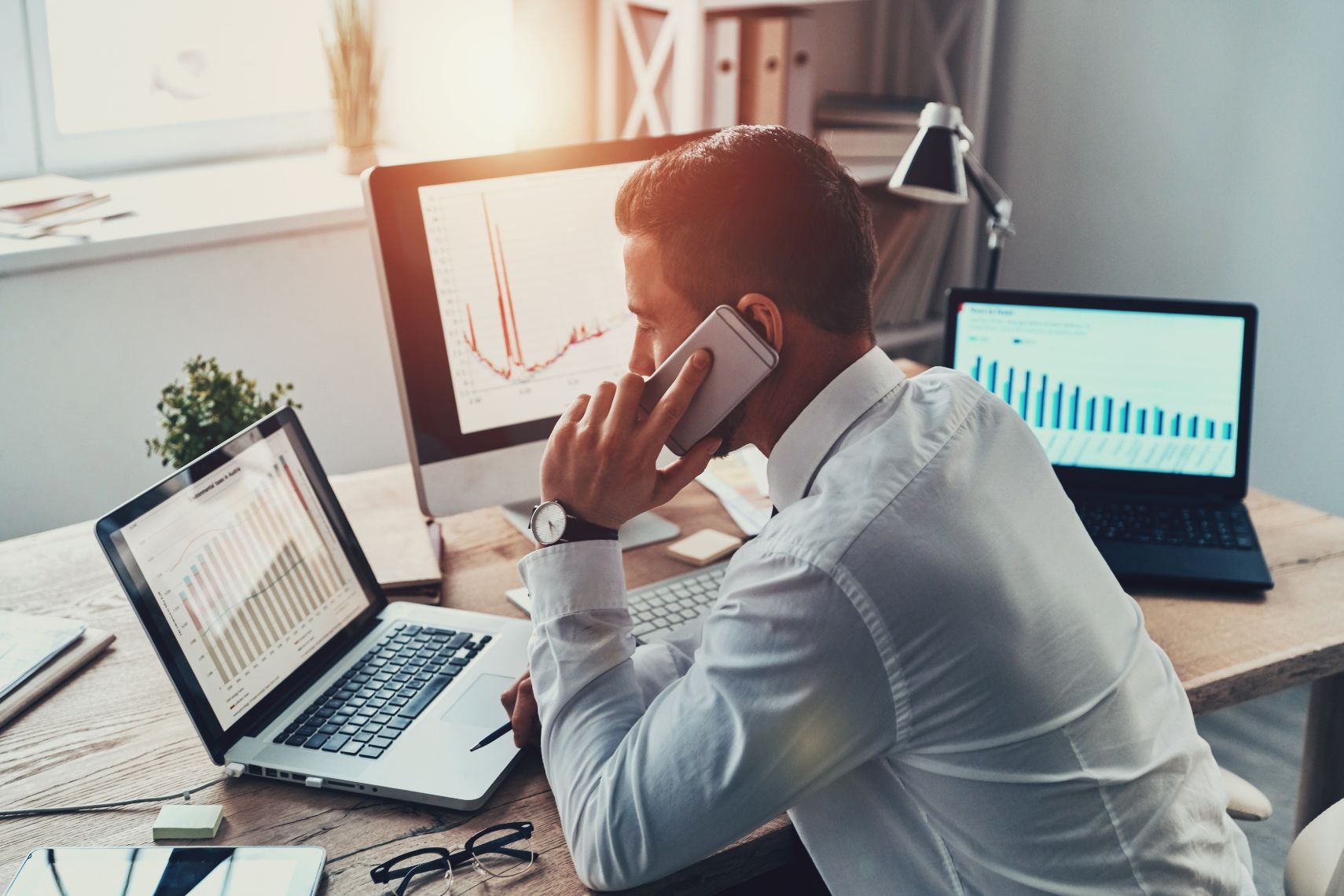 Business man on the phone while looking at multiple computer screens in an office