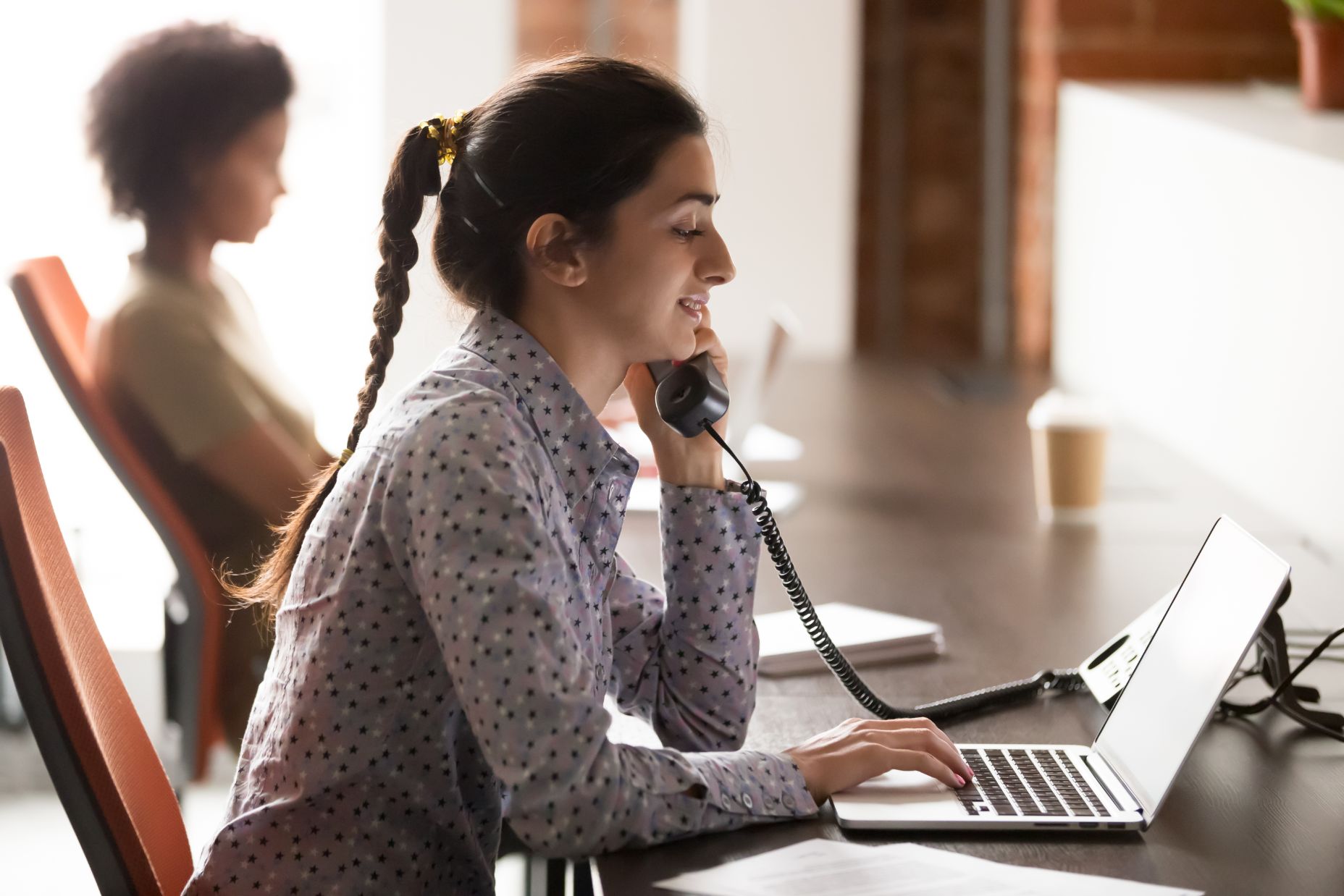 Business woman talking on phone sitting at a desk in an office