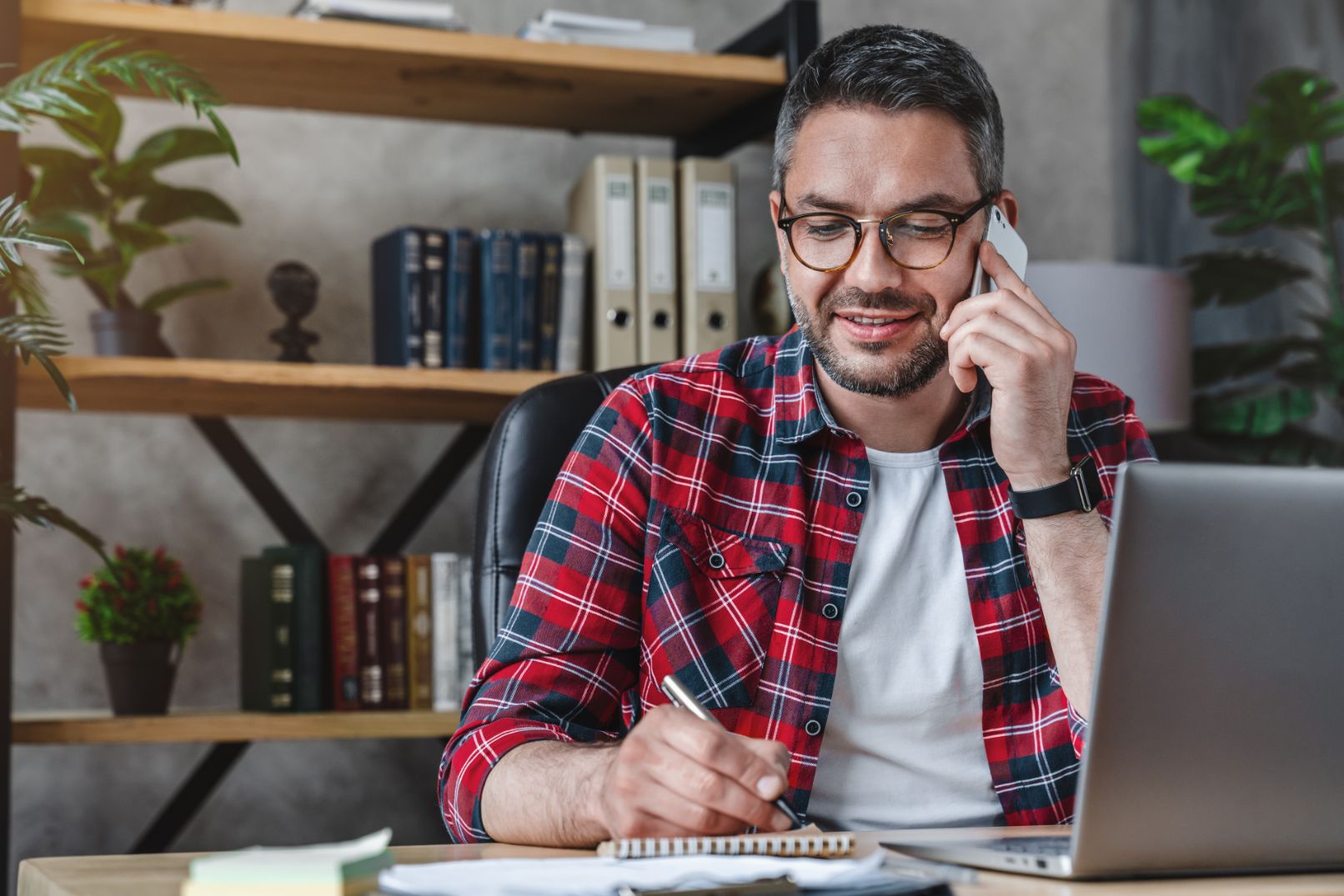 Buisness man working at desk writing notes while talking on phone