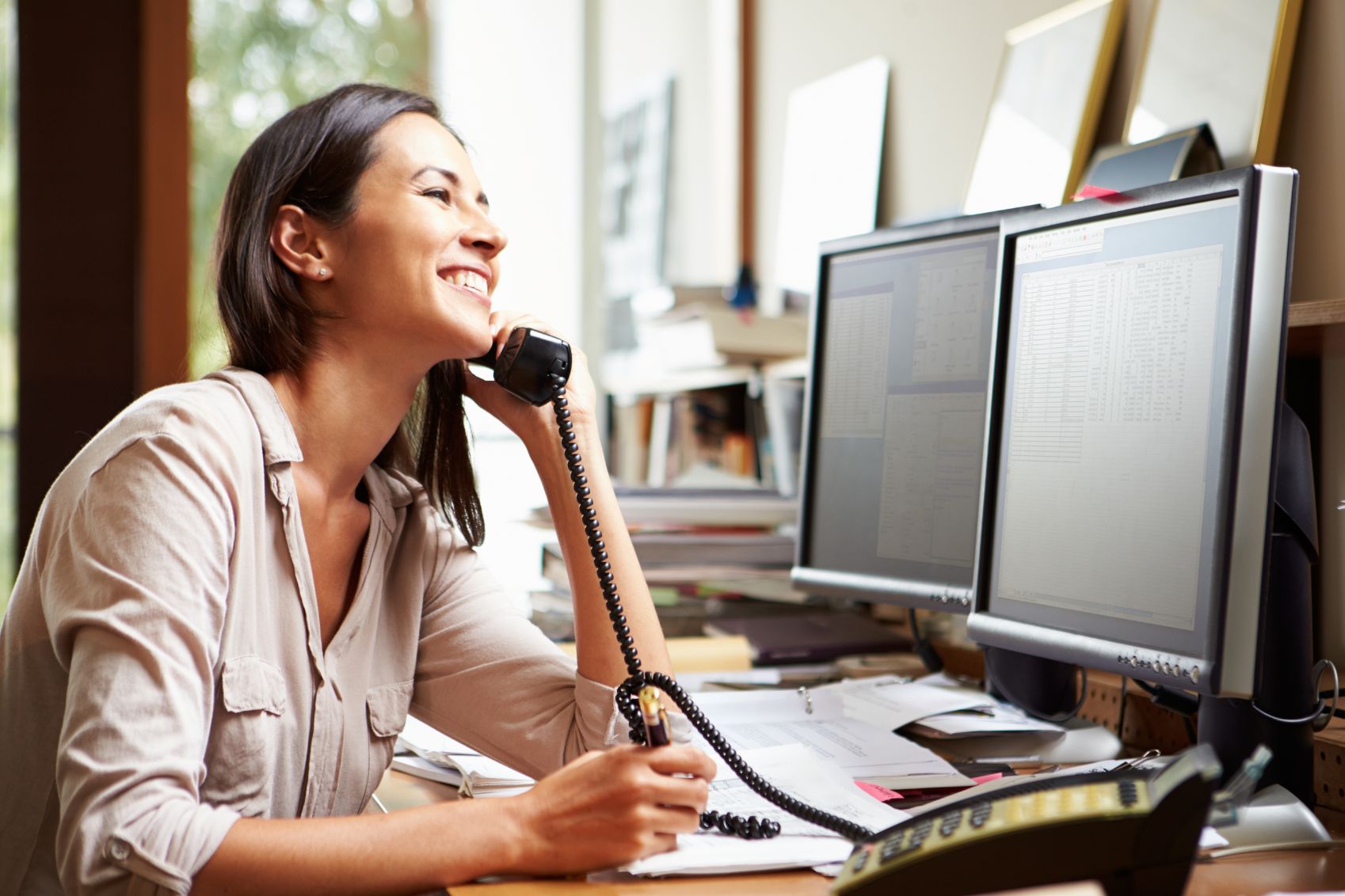 Woman talking on phone in office while looking at a computer