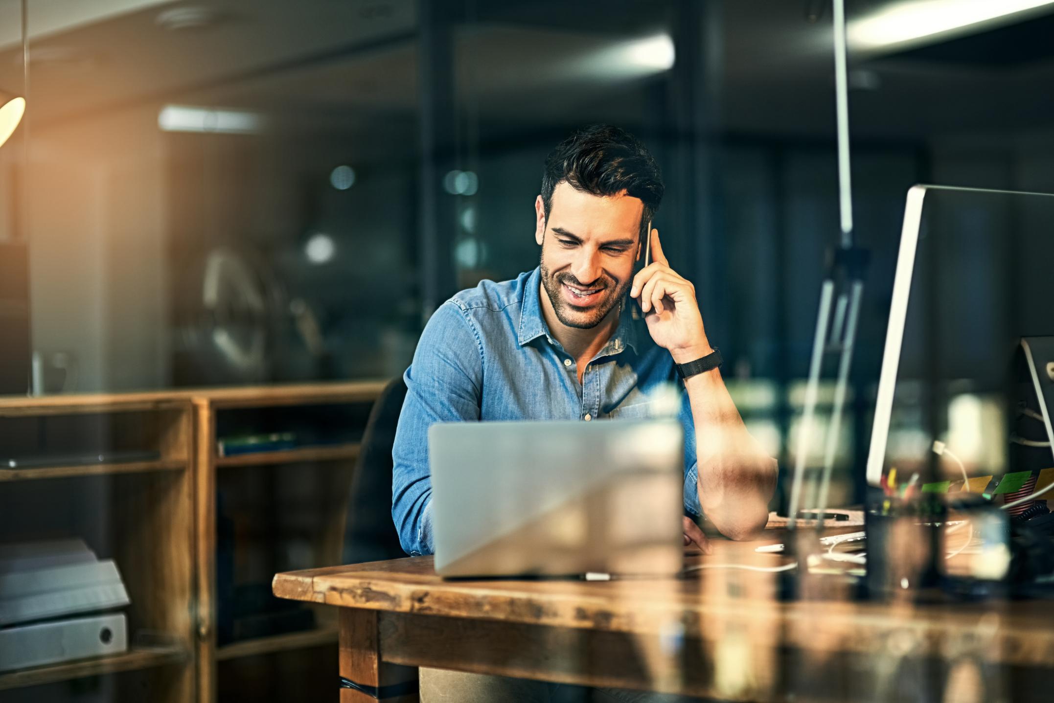 Business man talking on the phone while working on a laptop at a table