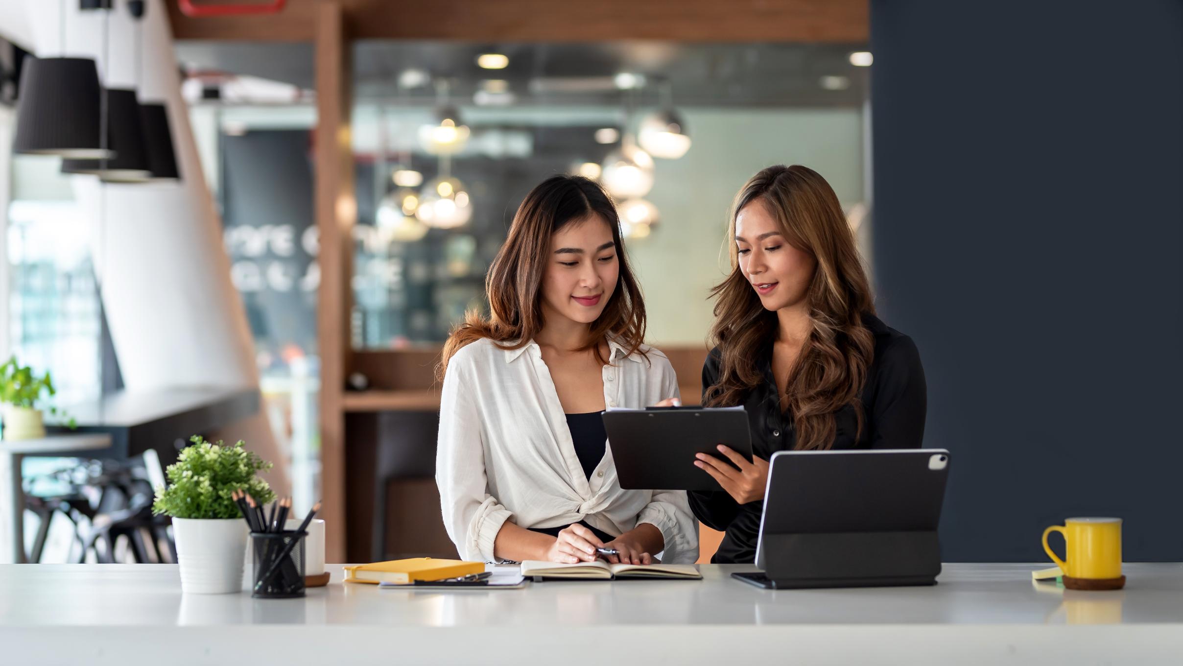 Two business woman working on computer and tablet at a desk