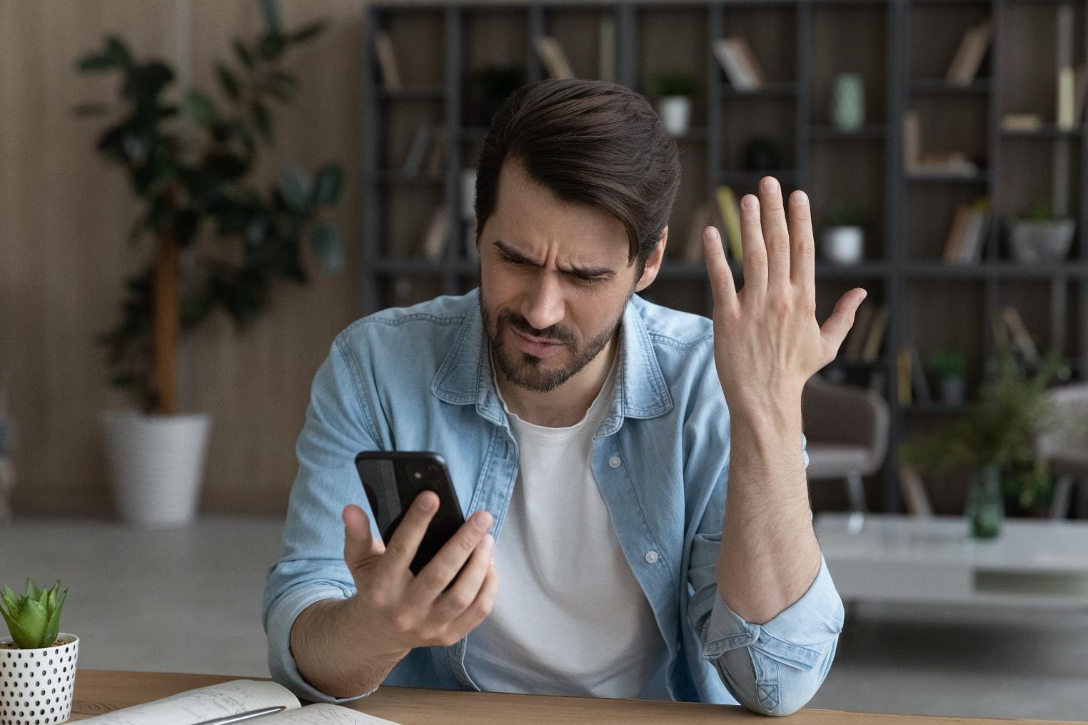 Person sitting at a desk frustrated while looking at their phone