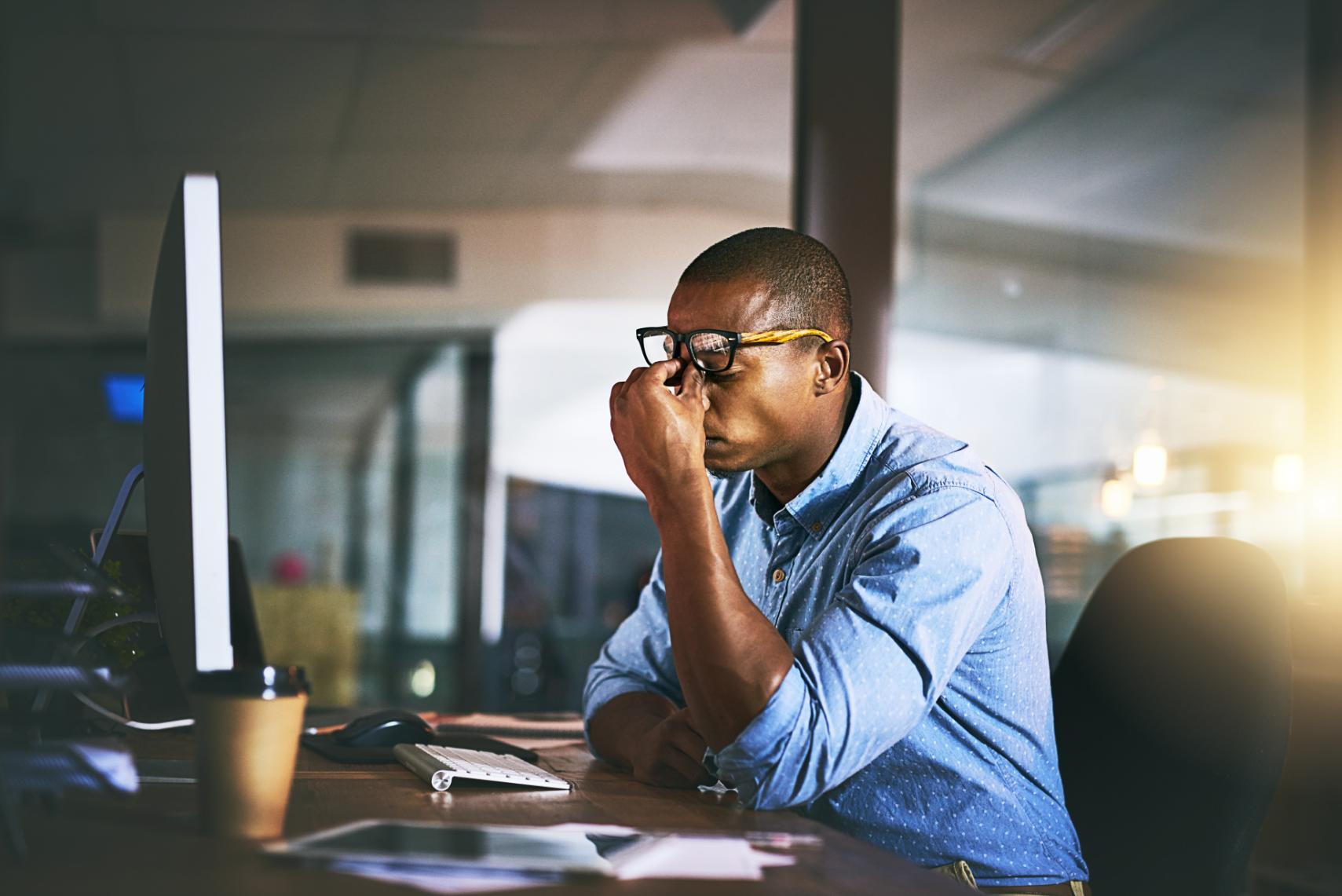 Frustrated business man sitting at a desk rubbing his eyes