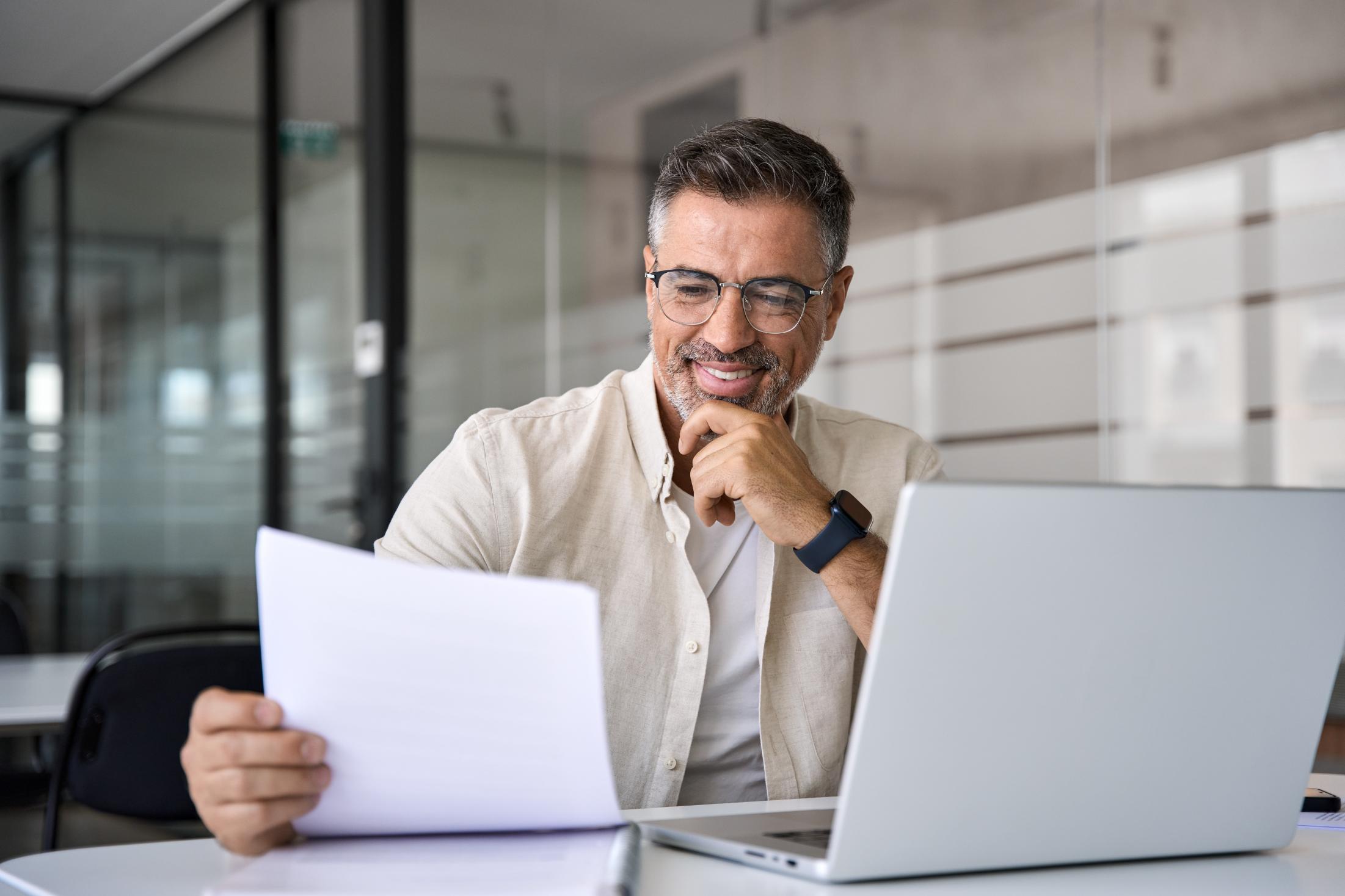 Business man working on computer and looking at sheet of paper