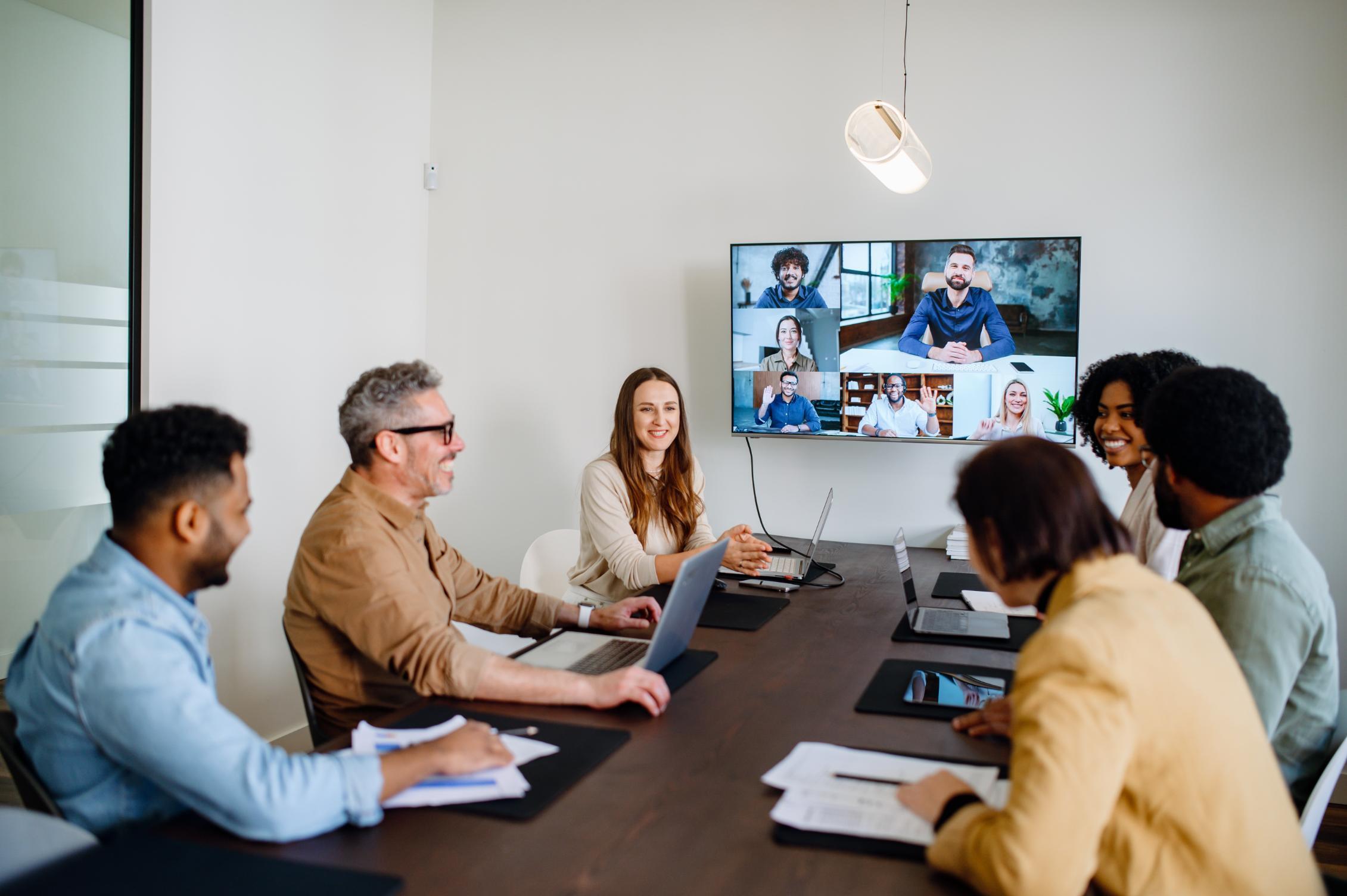 Group of employees working in a conference room while connecting with remote workers on the tv