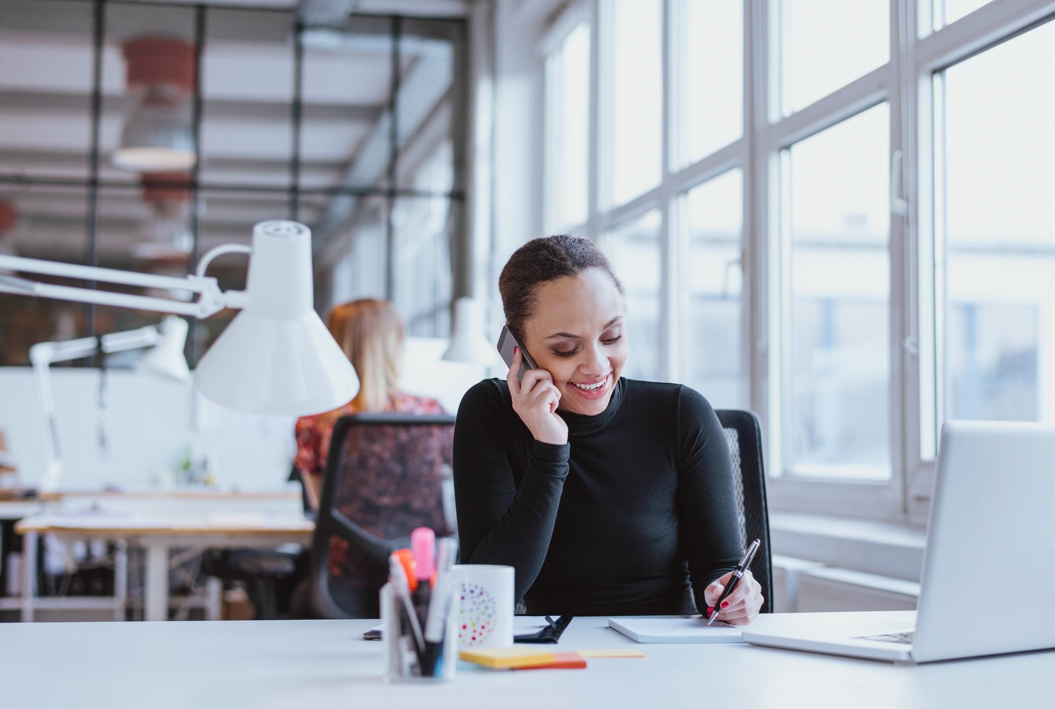 Business woman talking on the phone writing on notepad at desk