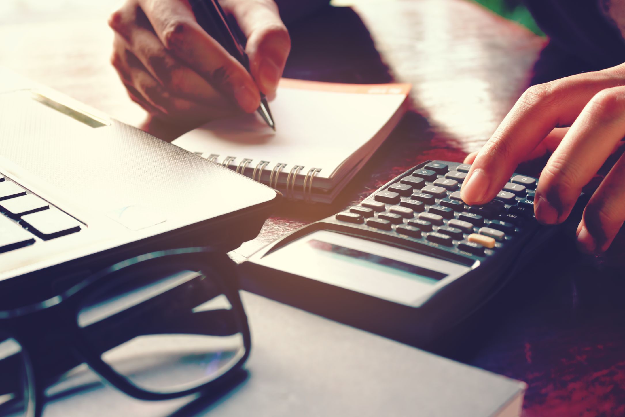 Person typing on calculator writing on a notepad