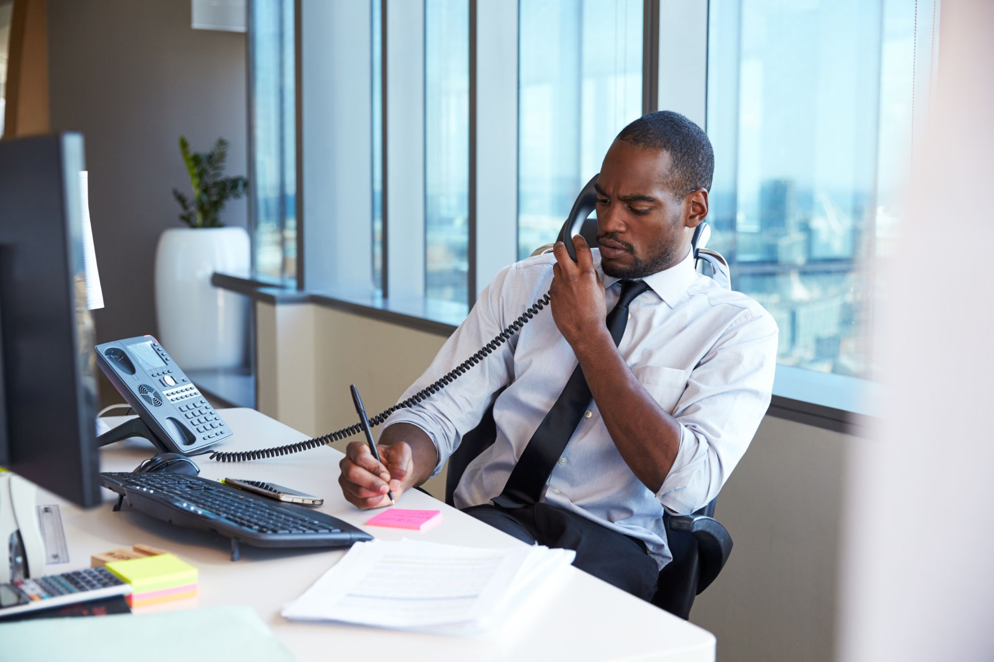 Business man talking on desk phone while writing notes 