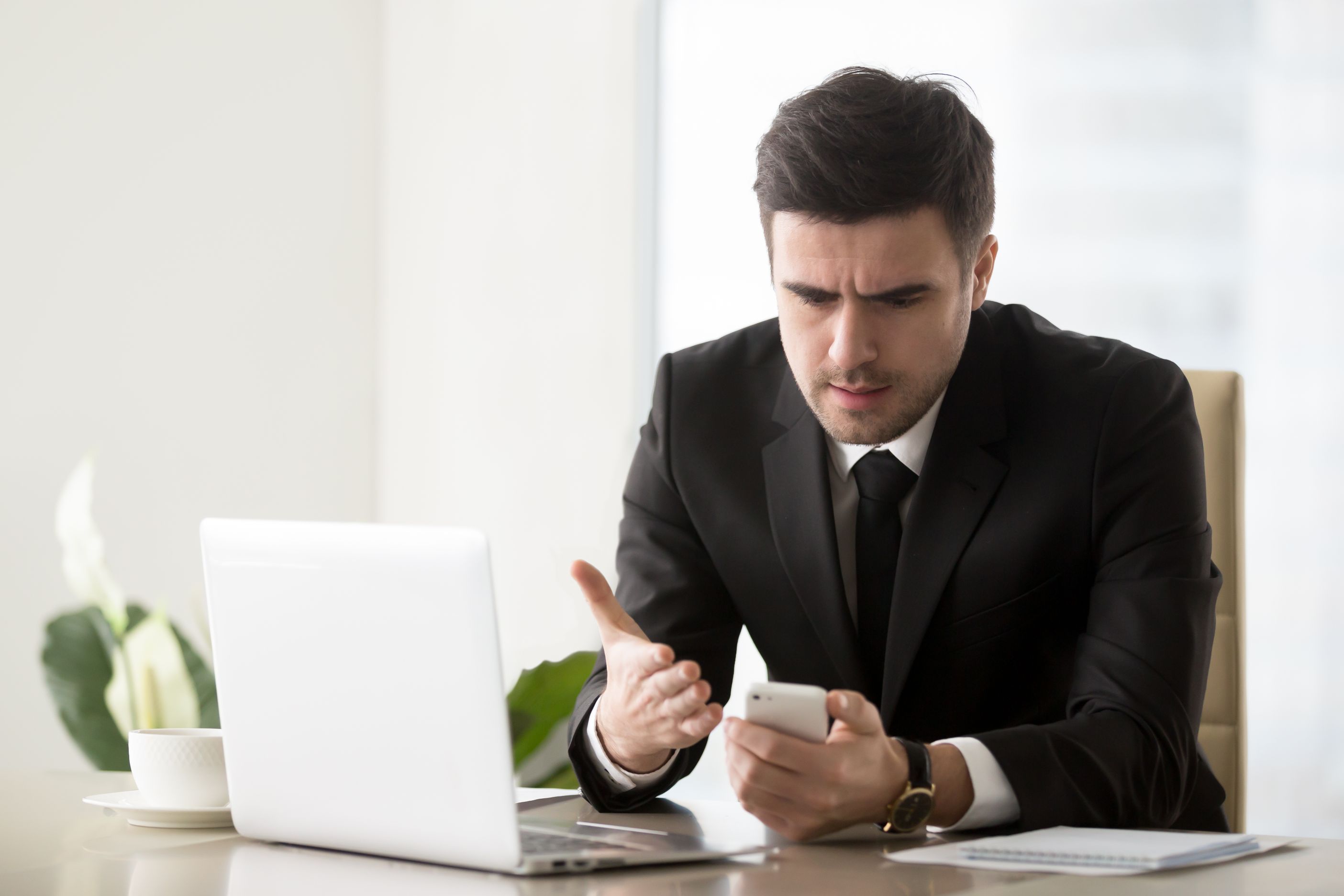 Frustrated businessman annoyed with phone call while working on laptop at a desk